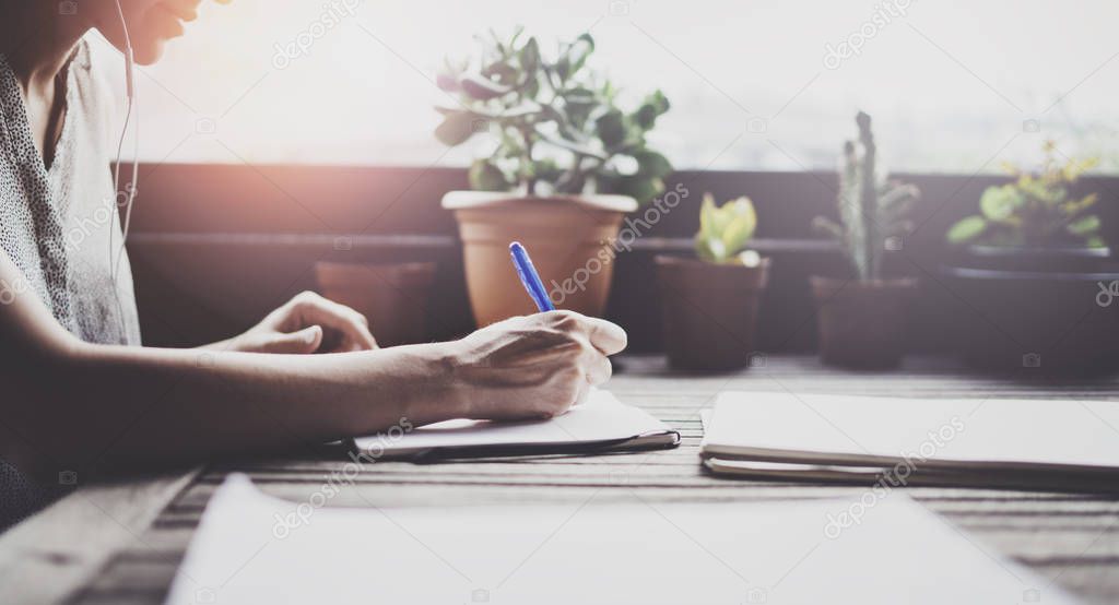 Young business woman sitting at table in caffee terrace and taking notes in notebook.On table is smartphone and paper documents. Student learning online or blogger concept.