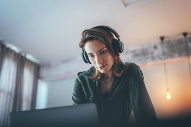 Modern evde rahatlayan, günlük kıyafetler giyen, akıllı telefondan müzik çalan ve kablosuz kulaklıkla ses kitapları dinleyen genç bir kız..