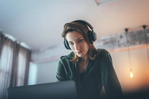 Young handsome girl relaxing at modern home,wearing casual clothes,playing music on smartphone and listening audio books in wireless headphones.Blurred background. — 스톡 사진