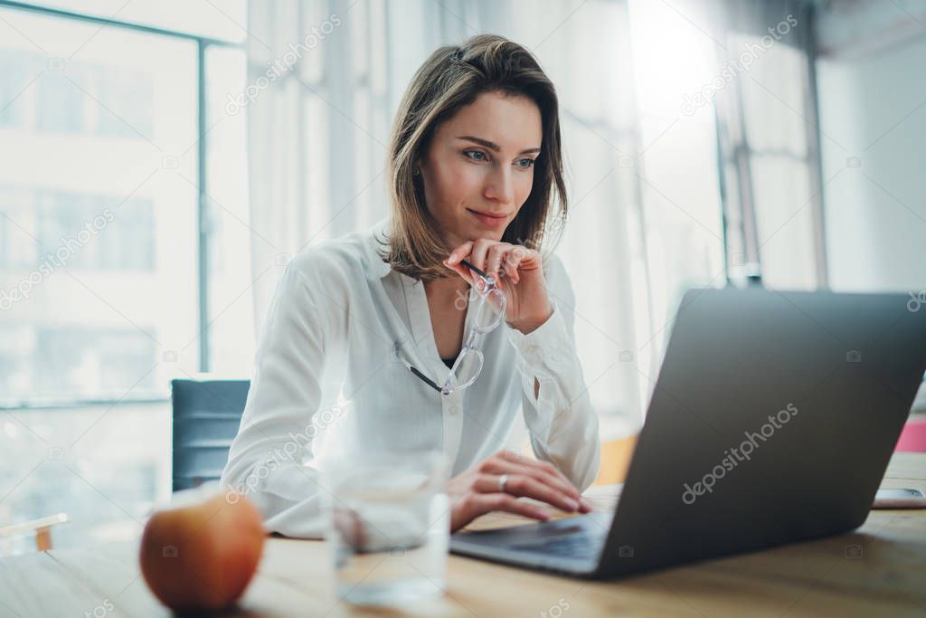 Confident businesswoman working on laptop at her workplace at modern office.Blurred background.