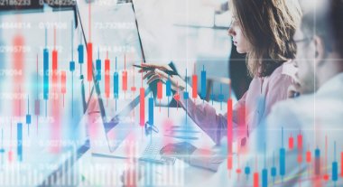 İş kadını ve onun collegue monitörde mali grafikler ve istatistikler ile ön dizüstü bilgisayar oturuyor. Çifte pozlama. Geniş.