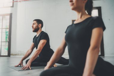 Yoga alıştırma sınıfı konsepti. Egzersiz yapan iki güzel insan. Genç kadın ve erkek içeride yoga yapıyor..