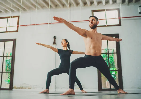 Los jóvenes deportistas practican ejercicios de yoga en el estudio. Pareja de jóvenes deportistas practicando clases de yoga con pareja — Foto de Stock