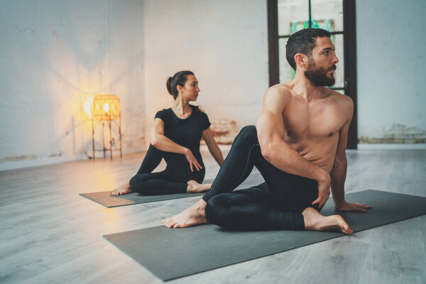 Концепция занятий йогой в классе. Молодая женщина и мужчина практикуют йогу в помещении. Два спортсмена делают упражнения. Лицензионные Стоковые Фото