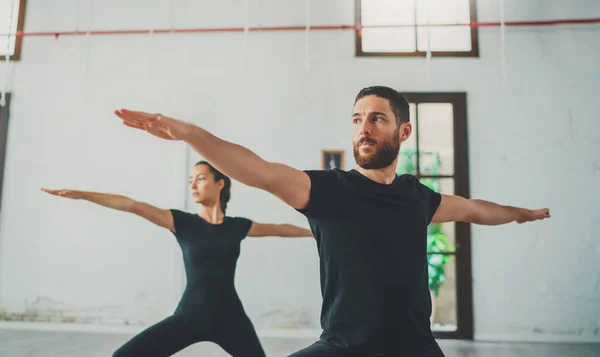 Young sportive man and woman are practicing yoga exercises in the studio. Couple of young sporty people practicing yoga lesson with partner — Stock Photo, Image