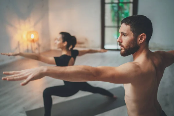 Jonge sportieve mannen en vrouwen oefenen yoga oefeningen in de studio. Paar jonge sportieve mensen oefenen yoga les met partner — Stockfoto