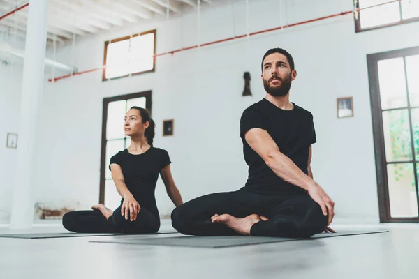 Yoga Pratica Esercizio Concetto di classe. Due belle persone che fanno esercizi. Giovane donna e uomo che praticano yoga al chiuso . Immagine Stock