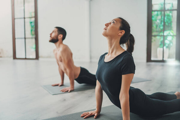 Молодой спортивный мужчина и женщина практикуют йогу упражнения в студии. Пара молодых спортсменов, практикующих йогу с партнером Стоковое Изображение