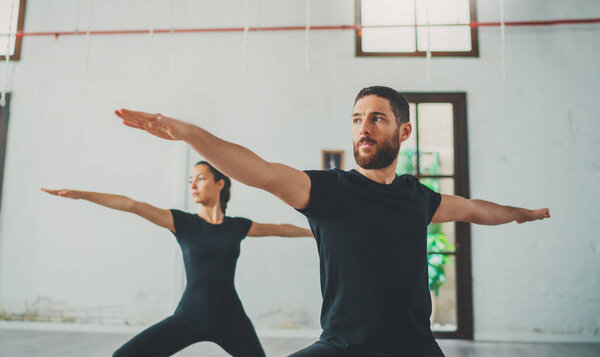 Молодой спортивный мужчина и женщина практикуют йогу упражнения в студии. Пара молодых спортсменов, практикующих йогу с партнером Лицензионные Стоковые Изображения