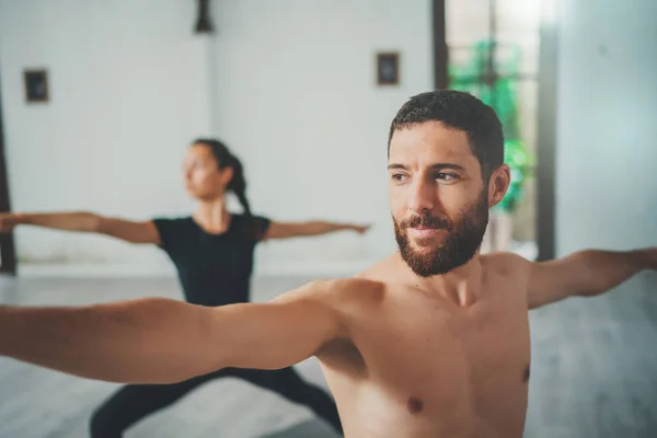 Young sportive man and woman are practicing yoga exercises in the studio. Couple of young sporty people practicing yoga lesson with partner — Stock Photo, Image