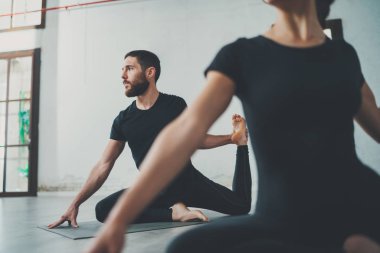 Yoga alıştırma sınıfı konsepti. Egzersiz yapan iki güzel insan. Genç kadın ve erkek içeride yoga yapıyor..
