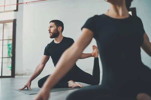 Concepto de clase de ejercicio de práctica de yoga. Dos personas hermosas haciendo ejercicios.Joven mujer y hombre practicando yoga en interiores . —  Fotos de Stock