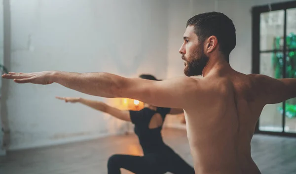 Giovani sportivi uomo e donna praticano esercizi di yoga in studio. Coppia di giovani sportivi che praticano lezione di yoga con il partner Fotografia Stock