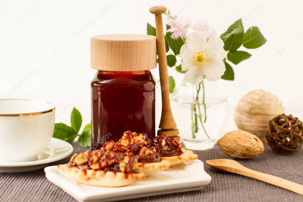 Jar  of dark honey on a table with flowers and other ingredients