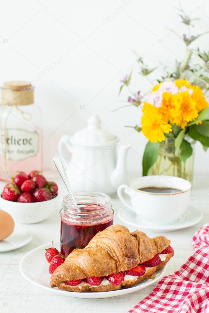 Breakfast with coffee, croissant and strawberry jam on a table