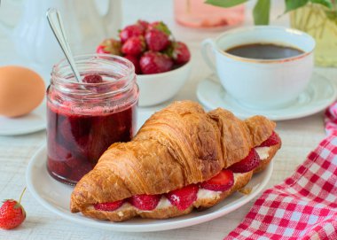 Kahve, kruvasan ve çilek reçeli bir tablo ile kahvaltı
