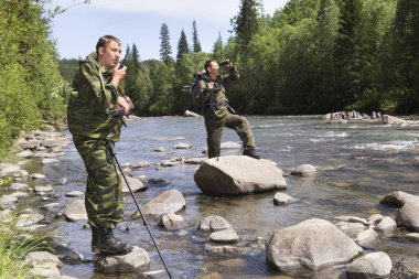 Forester ve mat sırtı ve trek bir tüfek arkasında dağ Nehri uyku Müfettiş bir sırt çantası ile orman içinde taşlar arasında akan