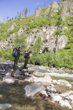 Forester ve mat sırtı ve trek bir tüfek arkasında dağ Nehri uyku Müfettiş bir sırt çantası ile orman içinde taşlar arasında akan