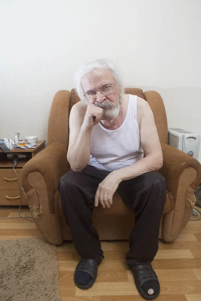 An old lonely sick poor man, suffering from eye disease with cataracts and glaucoma, sits in a chair all alone.