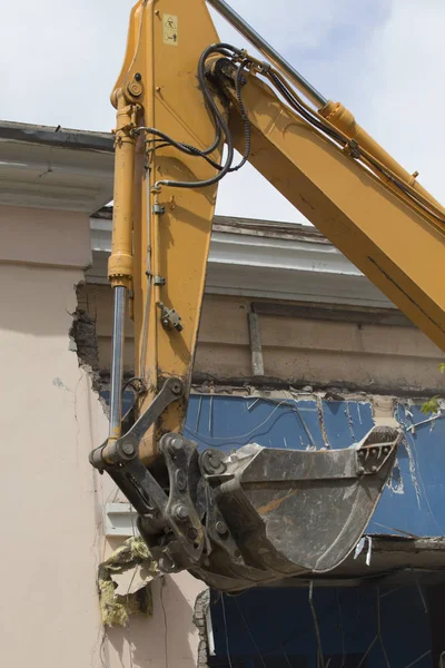 The destruction of the walls of the old building and the cleaning of construction debris with a bucket of an excavator.