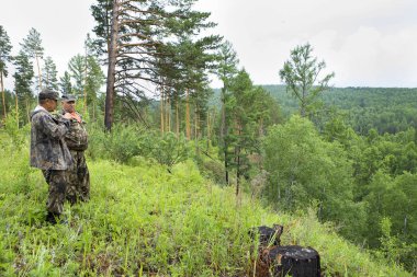Ormancılar orman koruma için gitti. Yetişkin bir erkek forester dağın zirvesine ormandan dürbün ile inceliyor. Avcı boz ayı habitat yönergeleri gösterir.