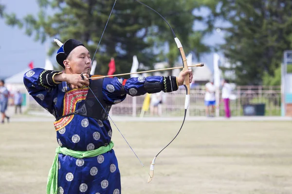 Competitions in shooting from a sports bow in Siberia. Mongolian competitions in archery. The sportsman is dressed in a traditional Buryat-Mongolian suit, shooting with his arrows during a national holiday.