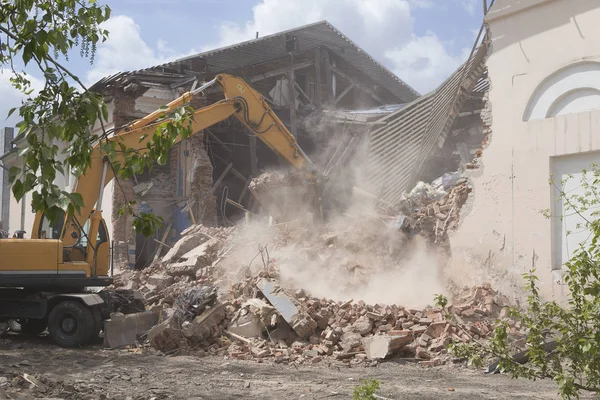 The destruction of the walls of the old building and the cleaning of construction debris with a bucket of an excavator.