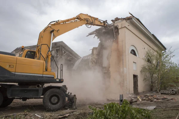 The destruction of the walls of the old building and the cleaning of construction debris with a bucket of an excavator.