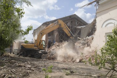 Eski binanın duvarlarının yıkılması ve bir kova kazıcıyla inşaat atıklarının temizlenmesi..