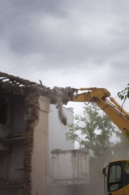 Eski binanın duvarlarının yıkılması ve bir kova kazıcıyla inşaat atıklarının temizlenmesi..