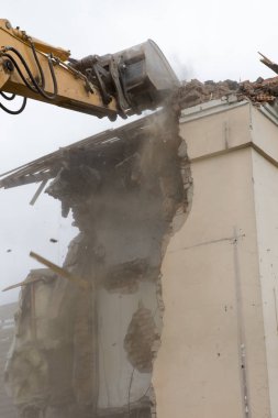 Eski binanın duvarlarının yıkılması ve bir kova kazıcıyla inşaat atıklarının temizlenmesi..
