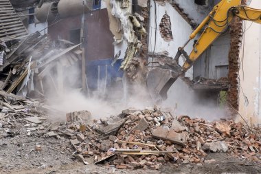 Eski binanın duvarlarının yıkılması ve bir kova kazıcıyla inşaat atıklarının temizlenmesi..