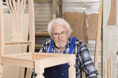 Ciddi mobilya Tasarımcısı dikkatle raf ahşap nesneleri ve onun arkasında desen ile onun ahşap atölyesinde üretim meşgul sandalye çerçeve parlatır