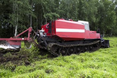 Patinaj traktörü yangın önleme şeridini açıyor. Patinaj traktörü bıçakla kesiyor ve en üst katmandaki toprağı çimlerle birlikte yığına yolluyor. Ormandaki yangınların önlenmesi.
