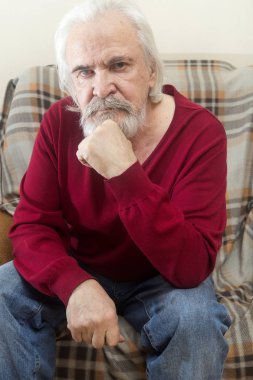 Yakışıklı bir hasta yaşlı adam sakallı ve bıyıklı bir bakım evinde uzun beyaz saçlı bir koltukta tek başına oturur ve son yıl yansıtır