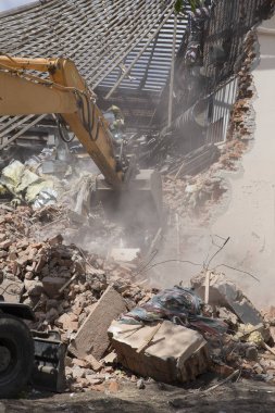 Eski binanın duvarlarının yıkılması ve bir kova kazıcıyla inşaat atıklarının temizlenmesi..