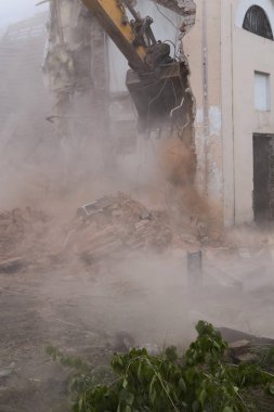 Eski binanın duvarlarının yıkılması ve bir kova kazıcıyla inşaat atıklarının temizlenmesi..