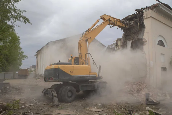 The destruction of the walls of the old building and the cleaning of construction debris with a bucket of an excavator.