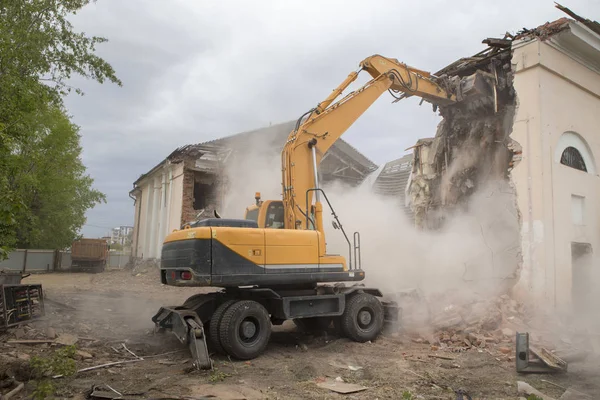 The destruction of the walls of the old building and the cleaning of construction debris with a bucket of an excavator.