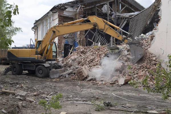 The destruction of the walls of the old building and the cleaning of construction debris with a bucket of an excavator.