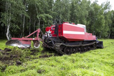 Patinaj traktörü yangın önleme şeridini açıyor. Patinaj traktörü bıçakla kesiyor ve en üst katmandaki toprağı çimlerle birlikte yığına yolluyor. Ormandaki yangınların önlenmesi.