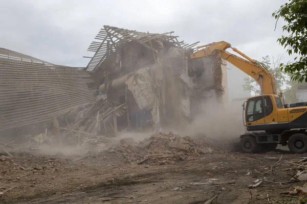 The destruction of the walls of the old building and the cleaning of construction debris with a bucket of an excavator.
