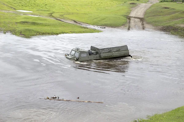 An off-road vehicle on leaves the river. The cross-country vehicle on the crosses the river. An off-road vehicle sails on the river.