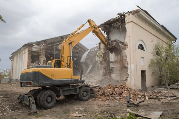 The destruction of the walls of the old building and the cleaning of construction debris with a bucket of an excavator.