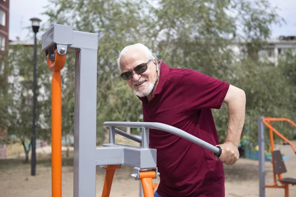 Senior man trains on sporting equipment on open air — Stock Photo, Image