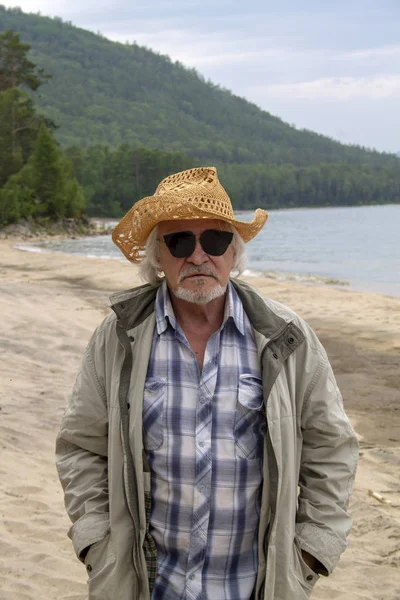 Старший чоловік у капелюсі сидить на березі — стокове фото