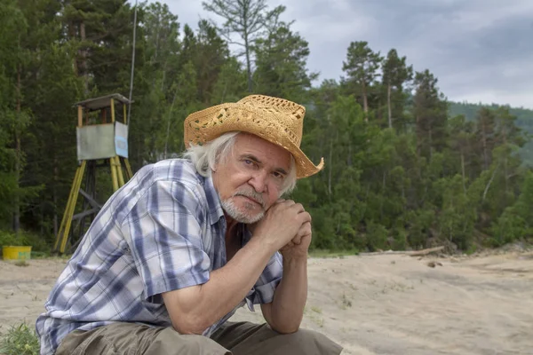 Старший чоловік у капелюсі сидить на березі — стокове фото