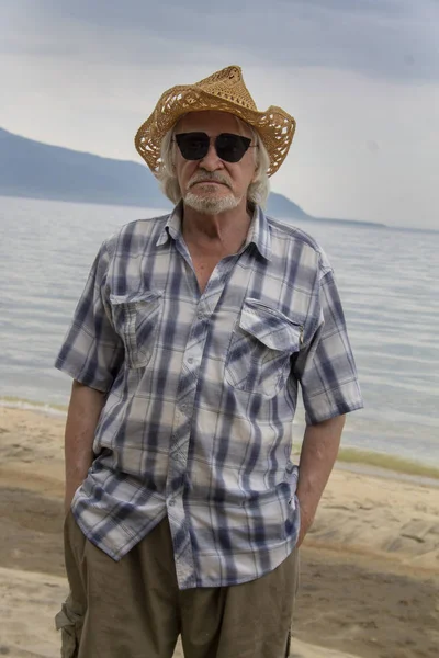 Senior man in a hat sits on the shore — ストック写真