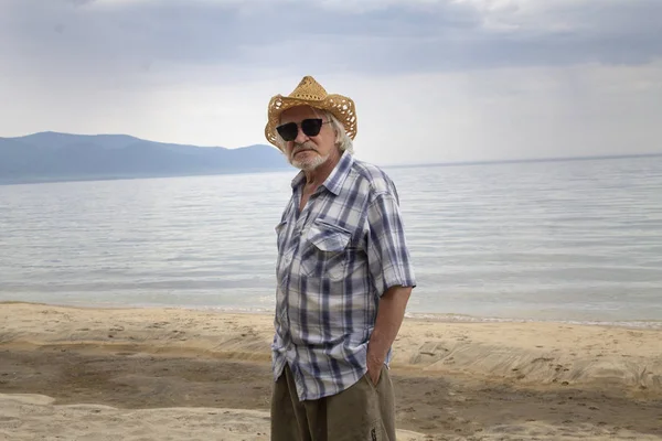 O homem sênior de chapéu senta-se na costa — Fotografia de Stock