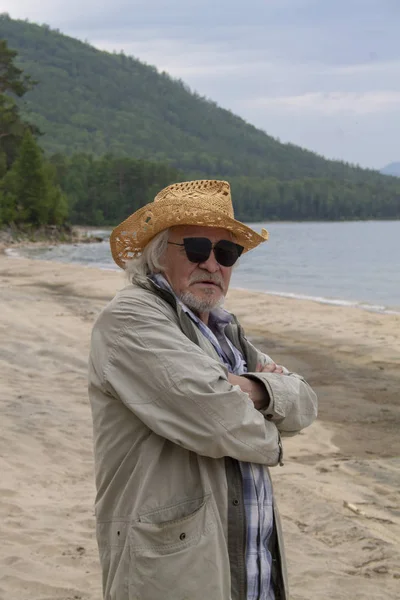 L'uomo anziano con un cappello si siede sulla riva — Foto Stock